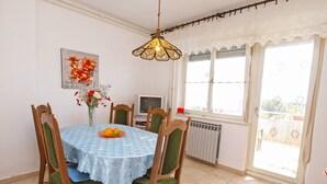 Un comedor con una mesa, sillas, un florero con flores, un televisor y una ventana con cortinas.