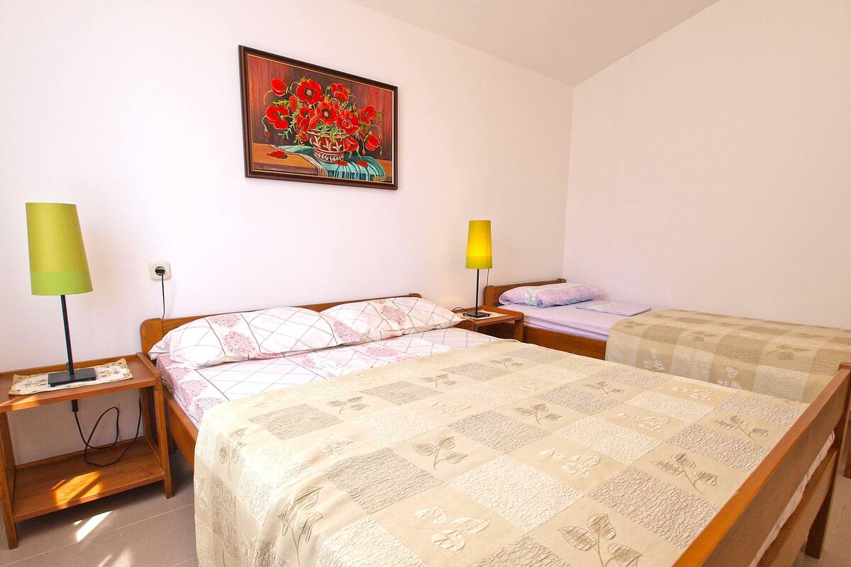 A hotel room with two beds, a nightstand with lamps, a painting on the wall, and a window.
