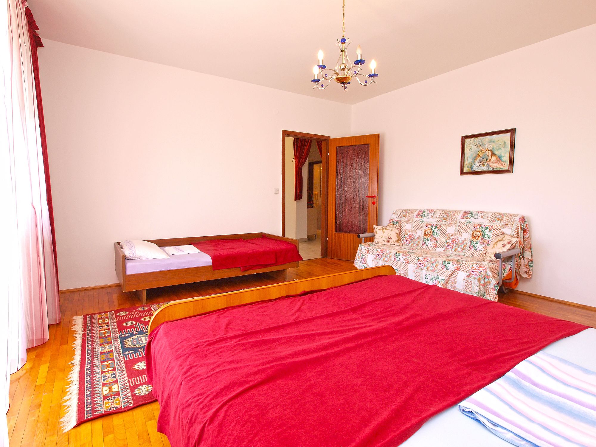 Un dormitorio con una cama grande, un sofá, una araña y un cuadro en la pared.