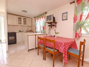 A kitchen with a dining area, featuring a stove, cabinets, a TV, and a clock on the wall. - Apartments Vladislava 906 (Liznjan)