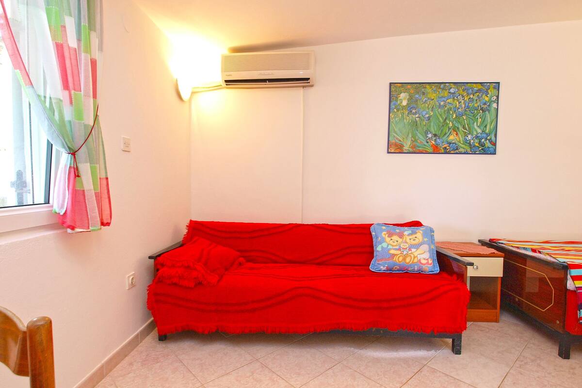A room with a red sofa, an air conditioning unit, a painting, and a window with curtains.