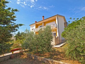 A two-story building with a balcony on the upper floor, surrounded by trees and vegetation.