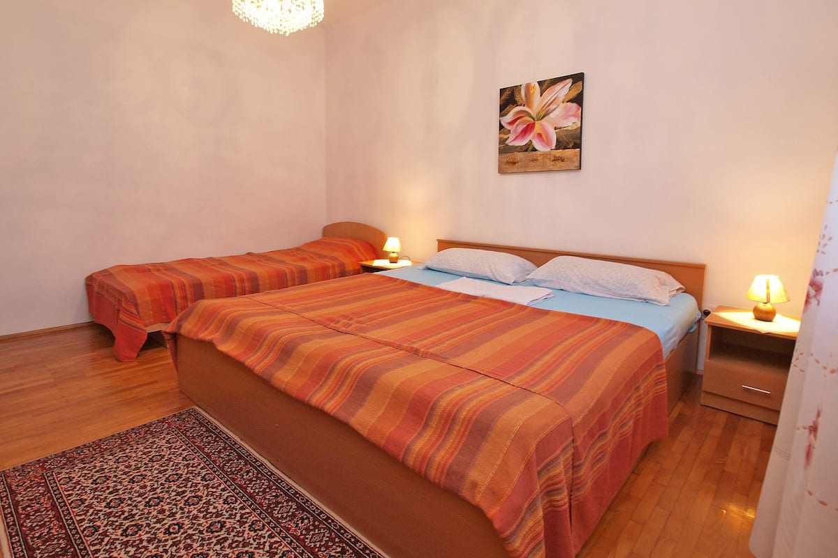 A hotel room with two beds, a chandelier, a painting, and a patterned rug.