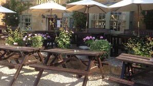 An outdoor seating area with wooden tables and umbrellas at the Crown & Trumpet establishment. - Crown and Trumpet Inn (Broadway)