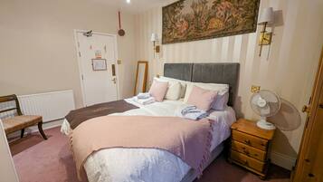 Un dormitorio con cama, mesita de noche, lámpara y un cuadro en la pared.