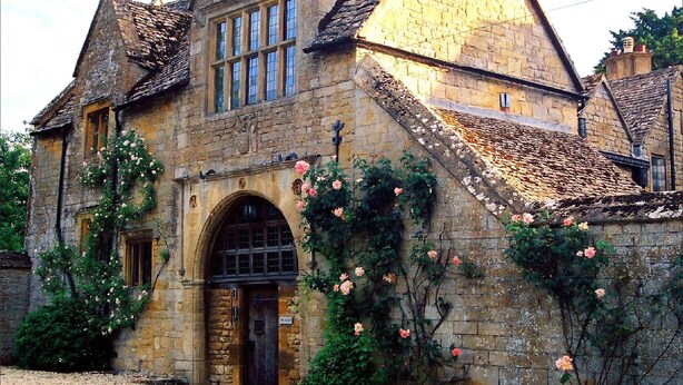 A historic stone building with a large arched entrance, multiple windows, and a steeply pitched roof. - Crown and Trumpet Inn (Broadway)