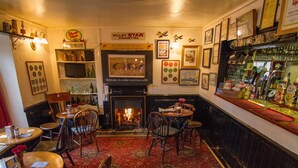 A cozy pub with a fireplace, wooden furniture, and a bar area with various bottles and glasses. - Crown and Trumpet Inn (Broadway)