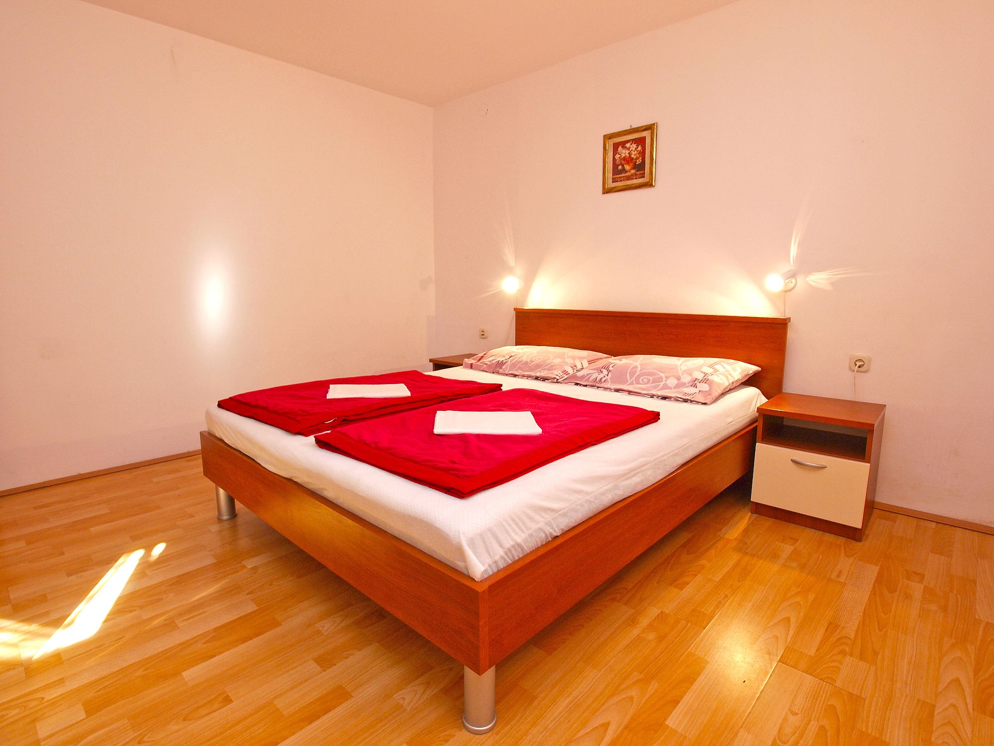 A double bed with red and white bedding, a wooden headboard, bedside tables, and a small bedside lamp.