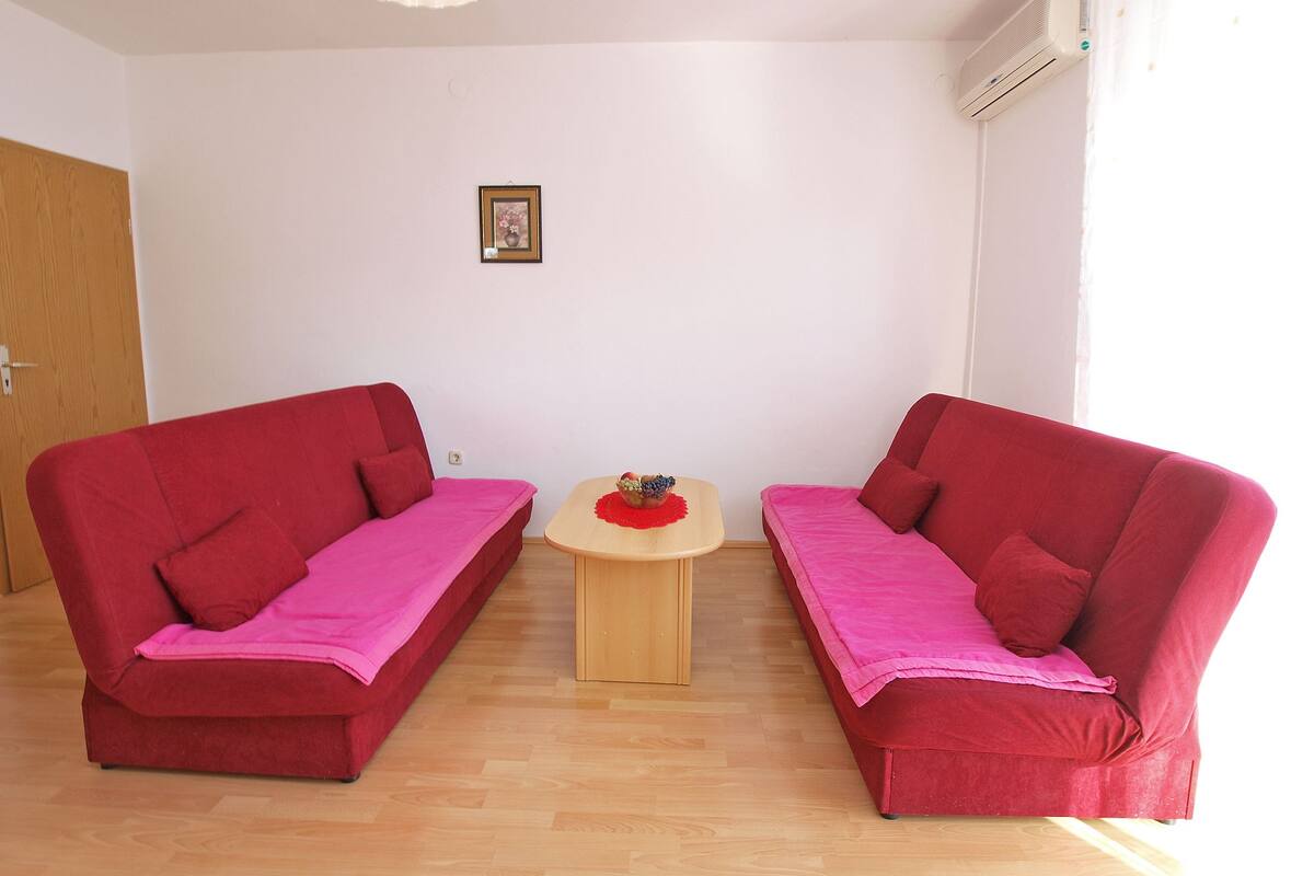 A room with two red sofas, a small wooden table with a bowl of fruit, and a framed picture on the wall.