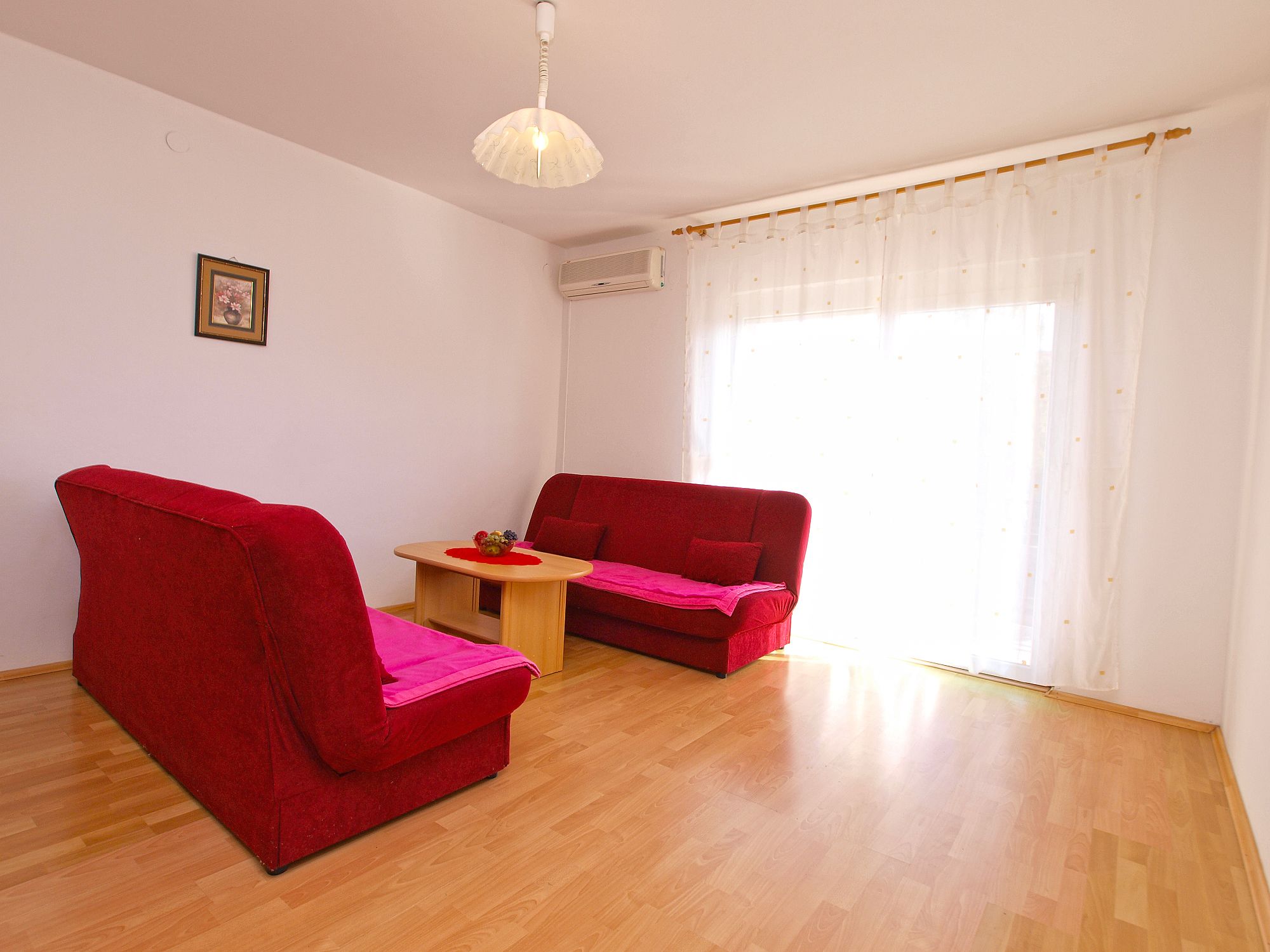 Una habitación con dos sofás rojos, una pequeña mesa de madera y una lámpara de techo blanca.