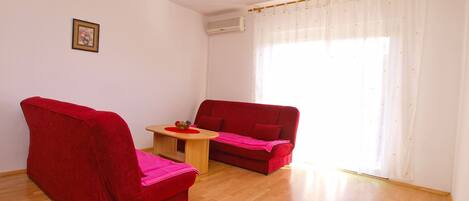 Una habitación con dos sofás rojos, una pequeña mesa de madera y una lámpara de techo blanca.