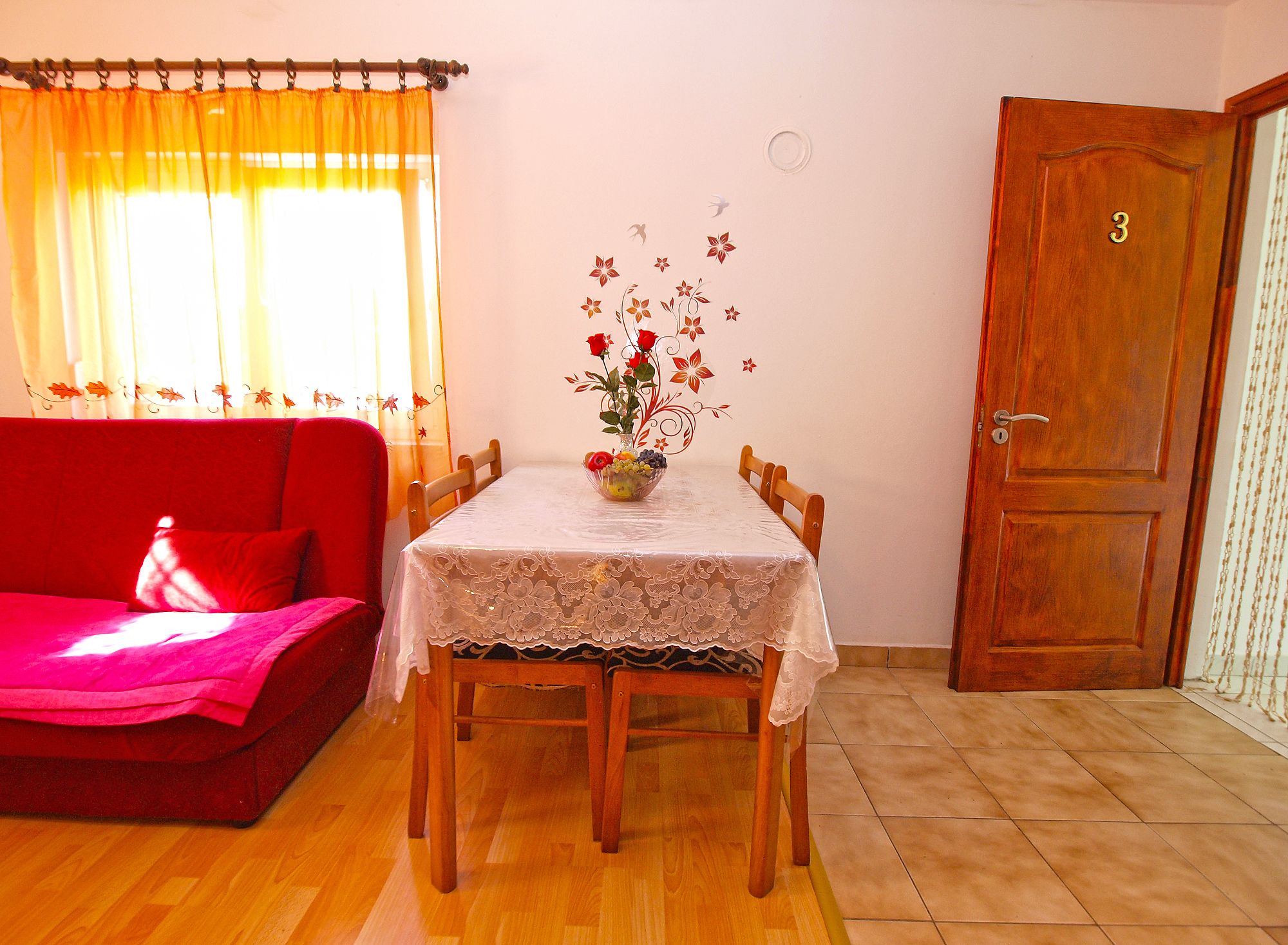 A dining area with a table set for four, a red sofa, and a wooden door with the number 3.