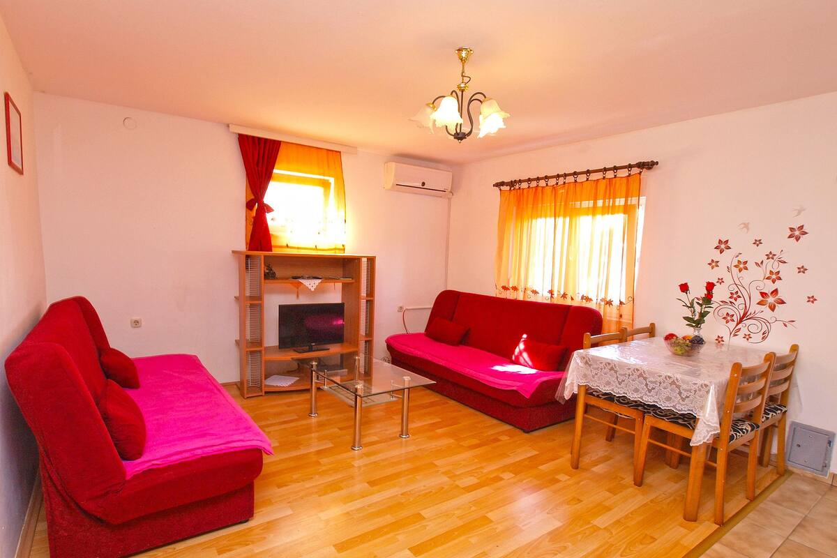 A living room with a red sofa, a glass coffee table, and a dining table with chairs.