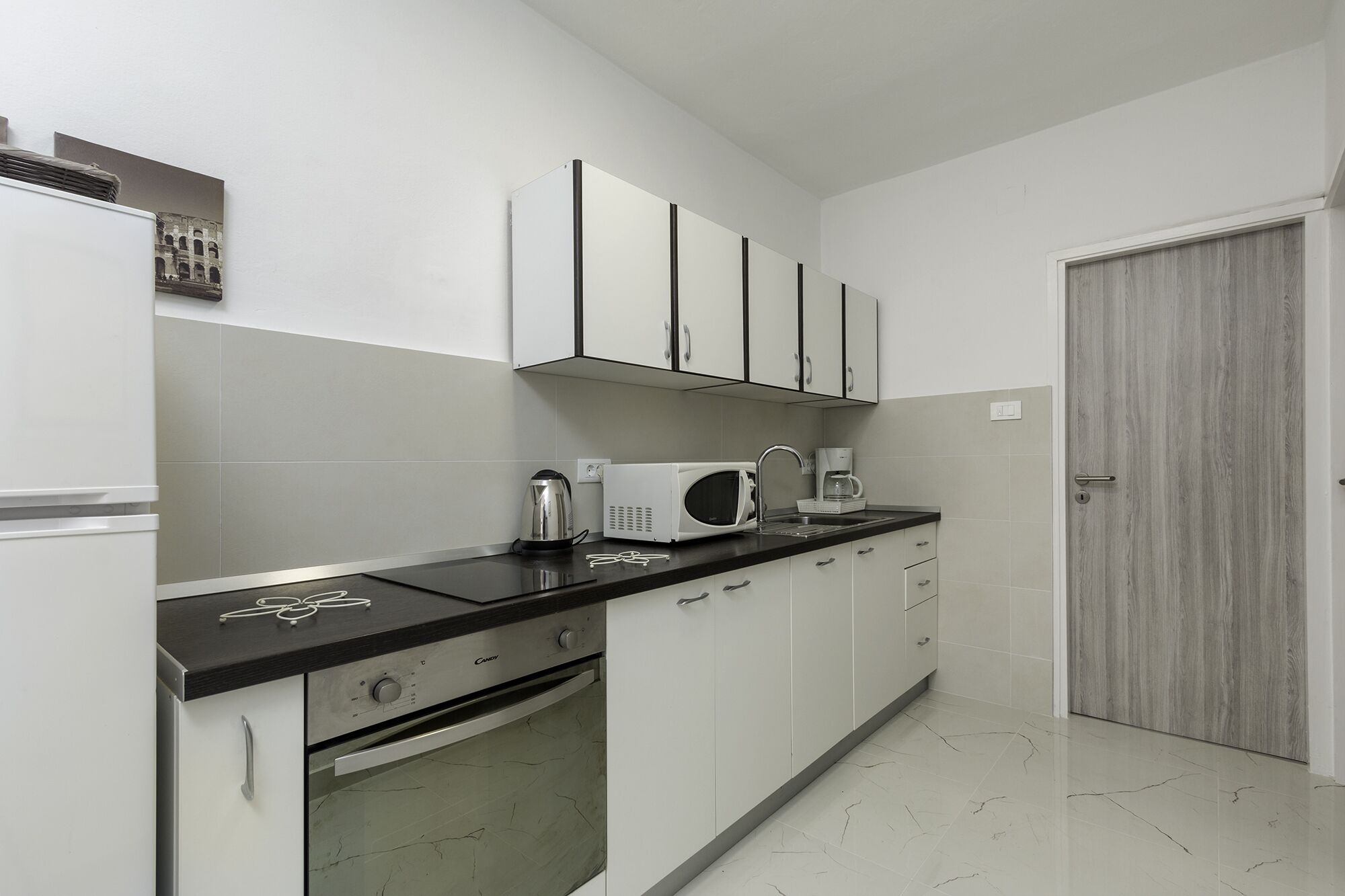 A kitchen with white cabinets, a black countertop, a microwave, a kettle, and a coffee maker.