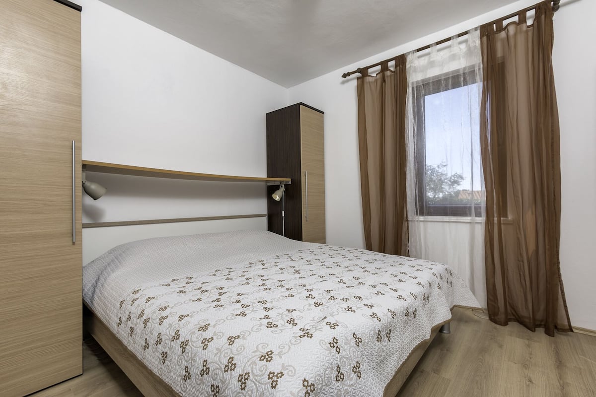 A bedroom with a bed, a wardrobe, a desk, and a window with curtains.