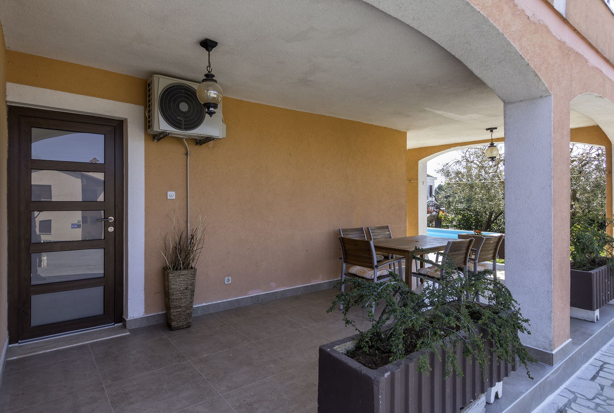 A covered outdoor area with a table and chairs, a potted plant, and a wall-mounted air conditioning unit.