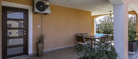 A covered outdoor area with a table and chairs, a potted plant, and a wall-mounted air conditioning unit.