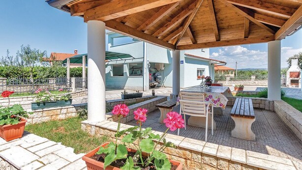 Un espacio al aire libre techado con techo de madera, pilares de piedra y patio de ladrillo.