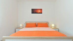Un dormitorio con una cama, dos mesitas de noche con lámparas y un cuadro colgado en la pared que representa un atardecer.