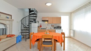 Una cocina compacta con una escalera de caracol, una mesa de comedor con manteles anaranjados y una ventana con cortinas.