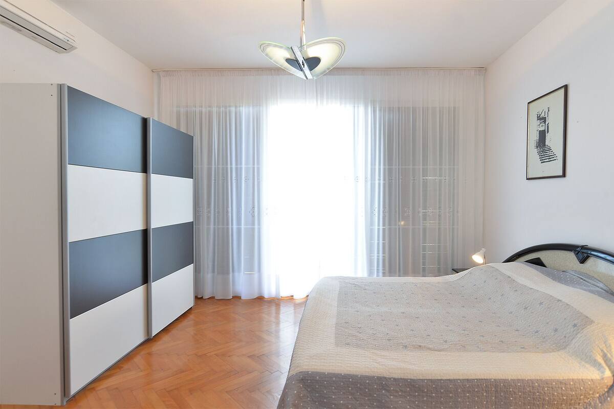 A bedroom with a bed, a wardrobe, a ceiling light, and a window with curtains.