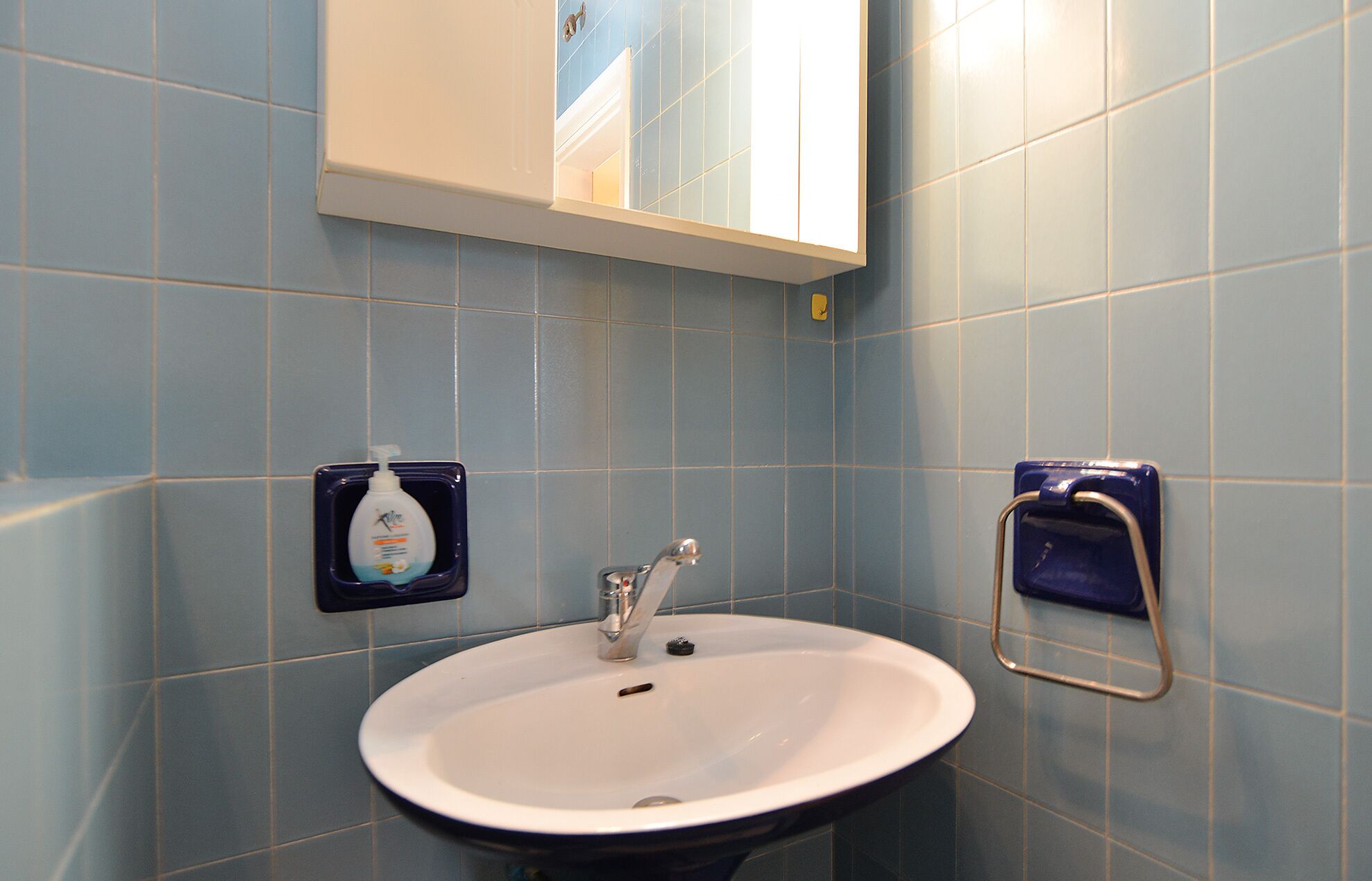 A bathroom with a white sink, blue tiles, a mirror, and a soap dispenser.