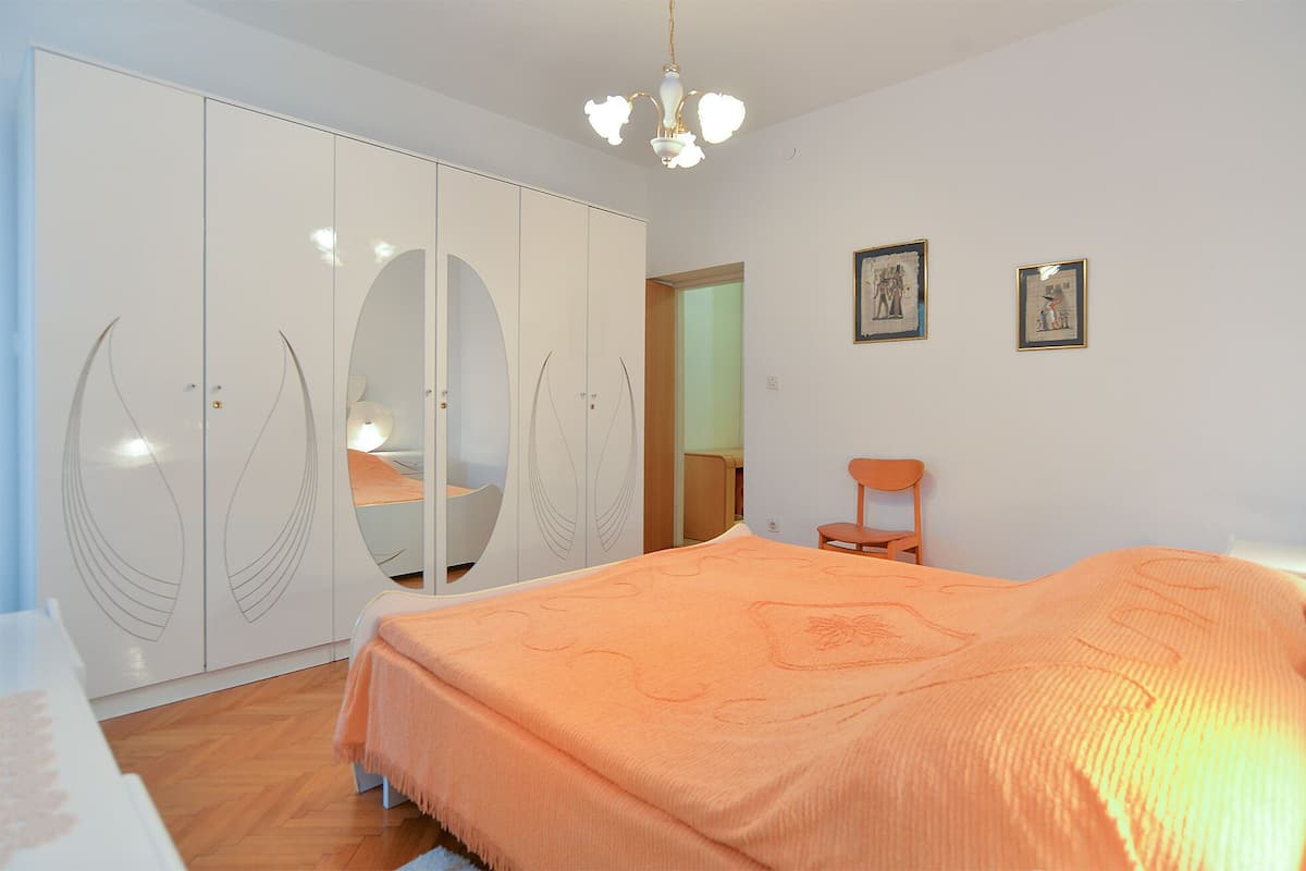 A bedroom with a bed, a wardrobe, a chair, and two framed pictures on the wall.
