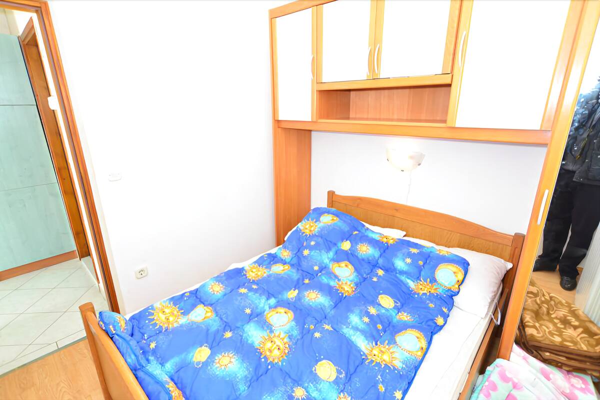 A small, single-bed room with a wooden headboard, a blue bedspread with sun and moon patterns, and a wooden wardrobe above the bed.
