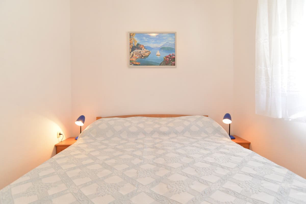 A bedroom with a bed, two bedside lamps, a painting on the wall, and a window with curtains.
