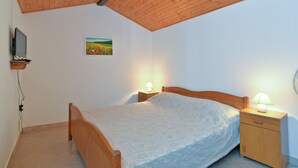 Un dormitori amb sostre de fusta, un llit amb col·cha estampada, dues taules de nit amb làmpades i una televisió penjada a la paret, a més d'un quadre petit.