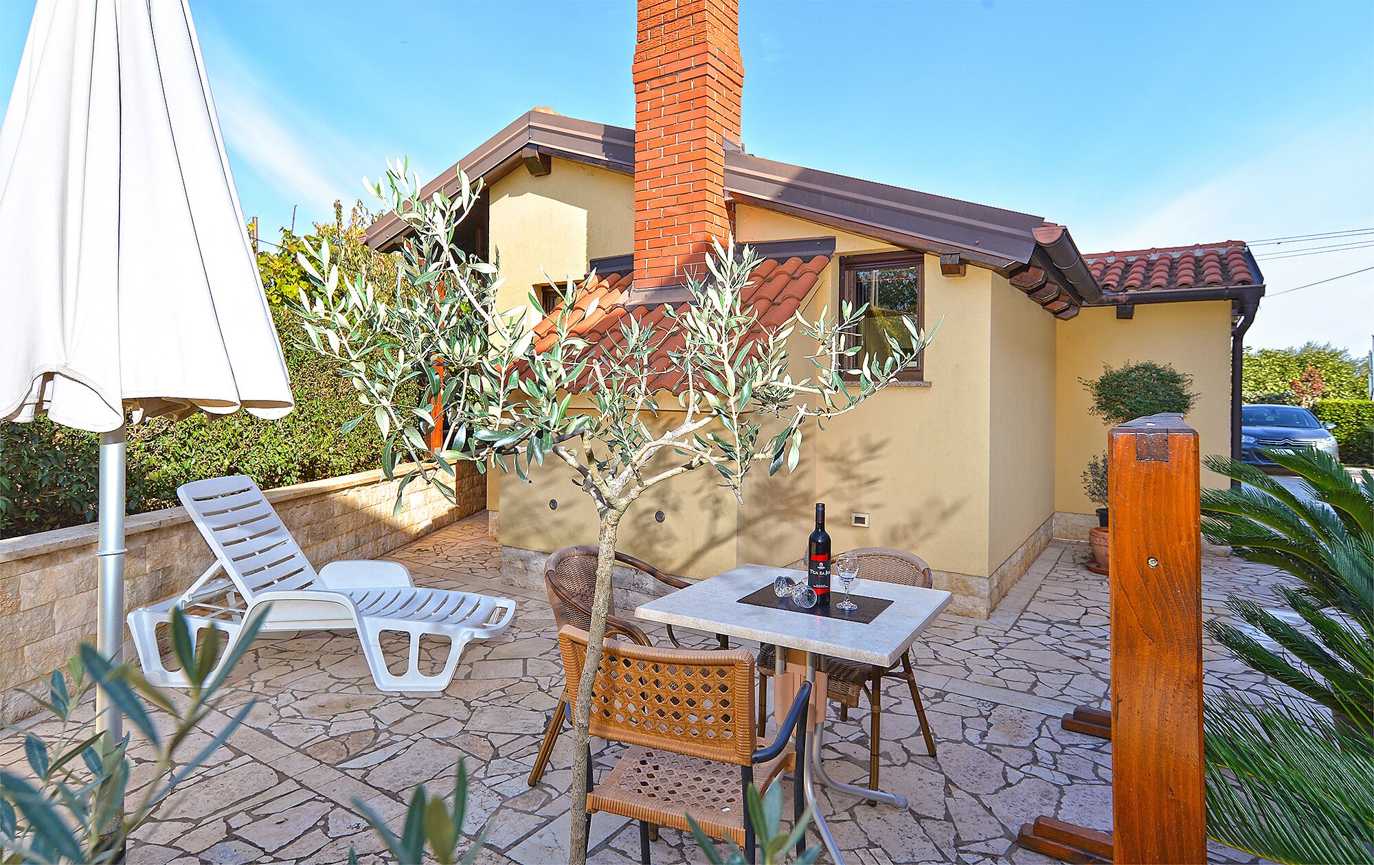 An outdoor patio with a table, chairs, and a bottle of wine.