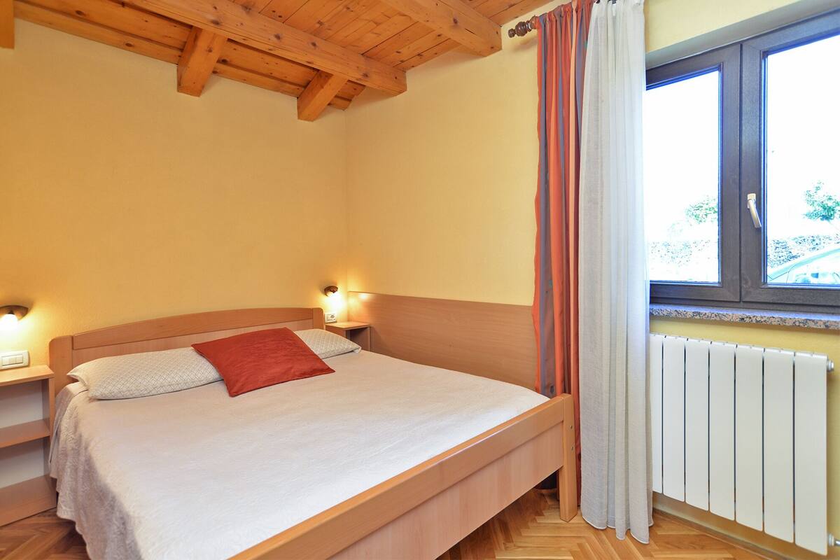 A bedroom with a wooden bed, a nightstand, a window with curtains, and a radiator.