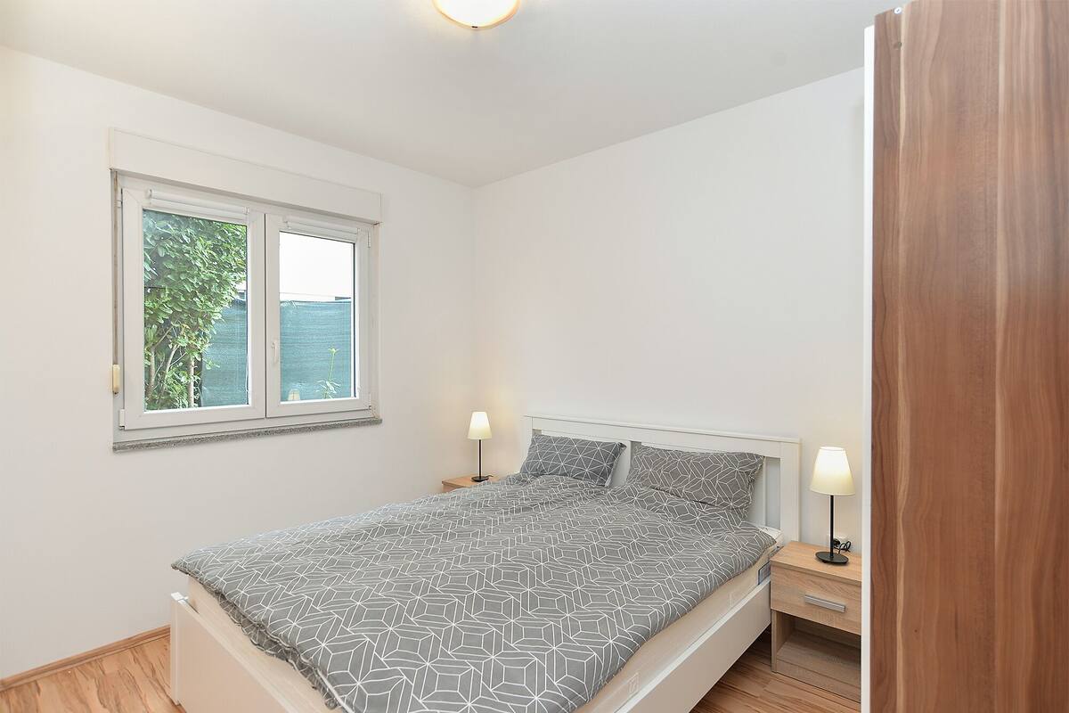 Un dormitorio con cama, mesitas de noche, ventana y puerta.