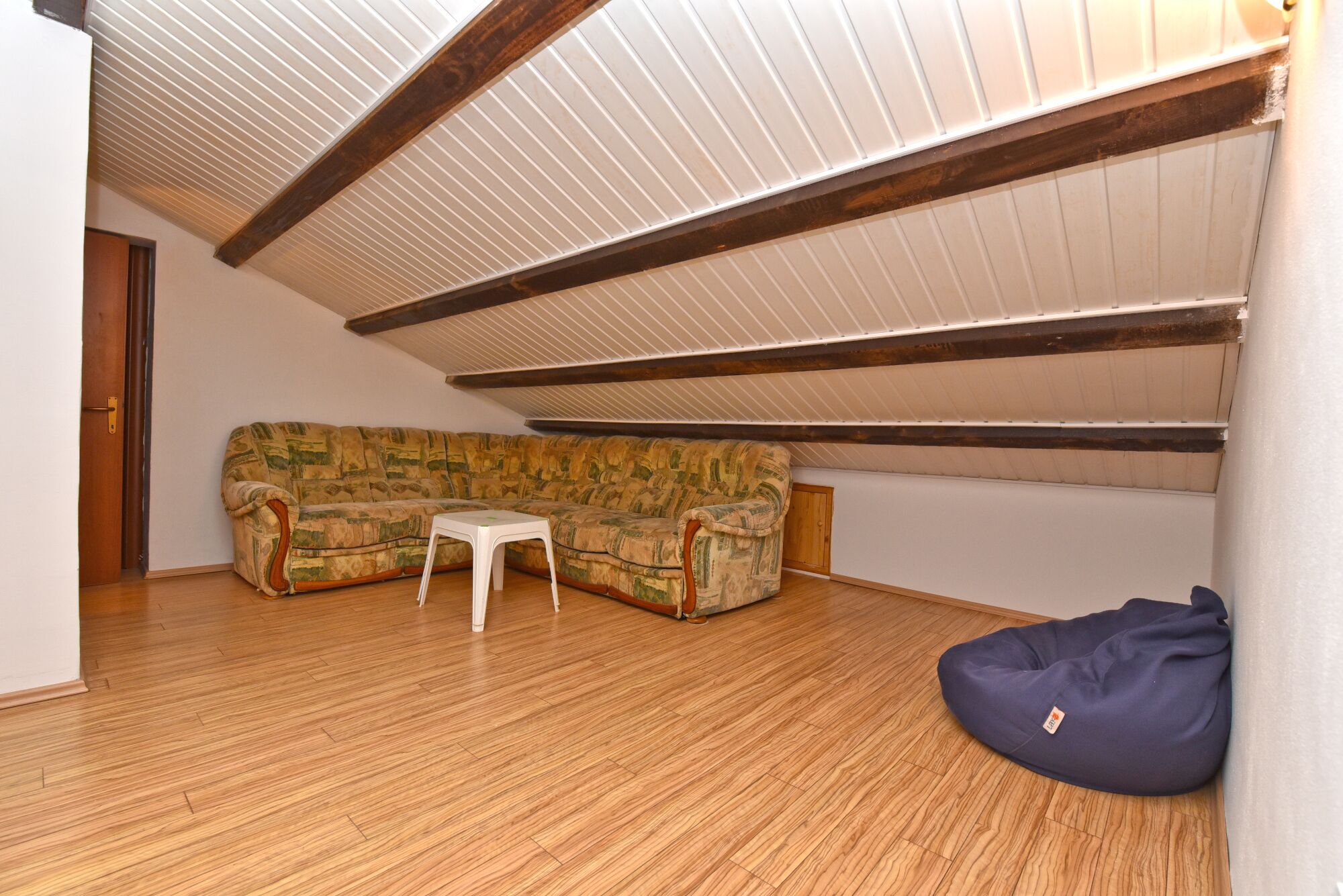 Ein Zimmer mit Holzboden, einem gemusterten Sofa, einem kleinen weißen Tisch und einem Sitzsack.