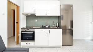 Cocina compacta con armarios blancos, refrigerador de acero inoxidable, horno empotrado y estufa a gas.