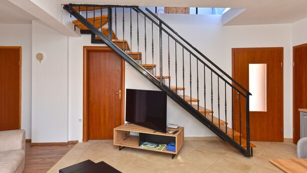 Una sala de estar moderna con una escalera de madera, un televisor de pantalla plana sobre un mueble de madera y un sofá.