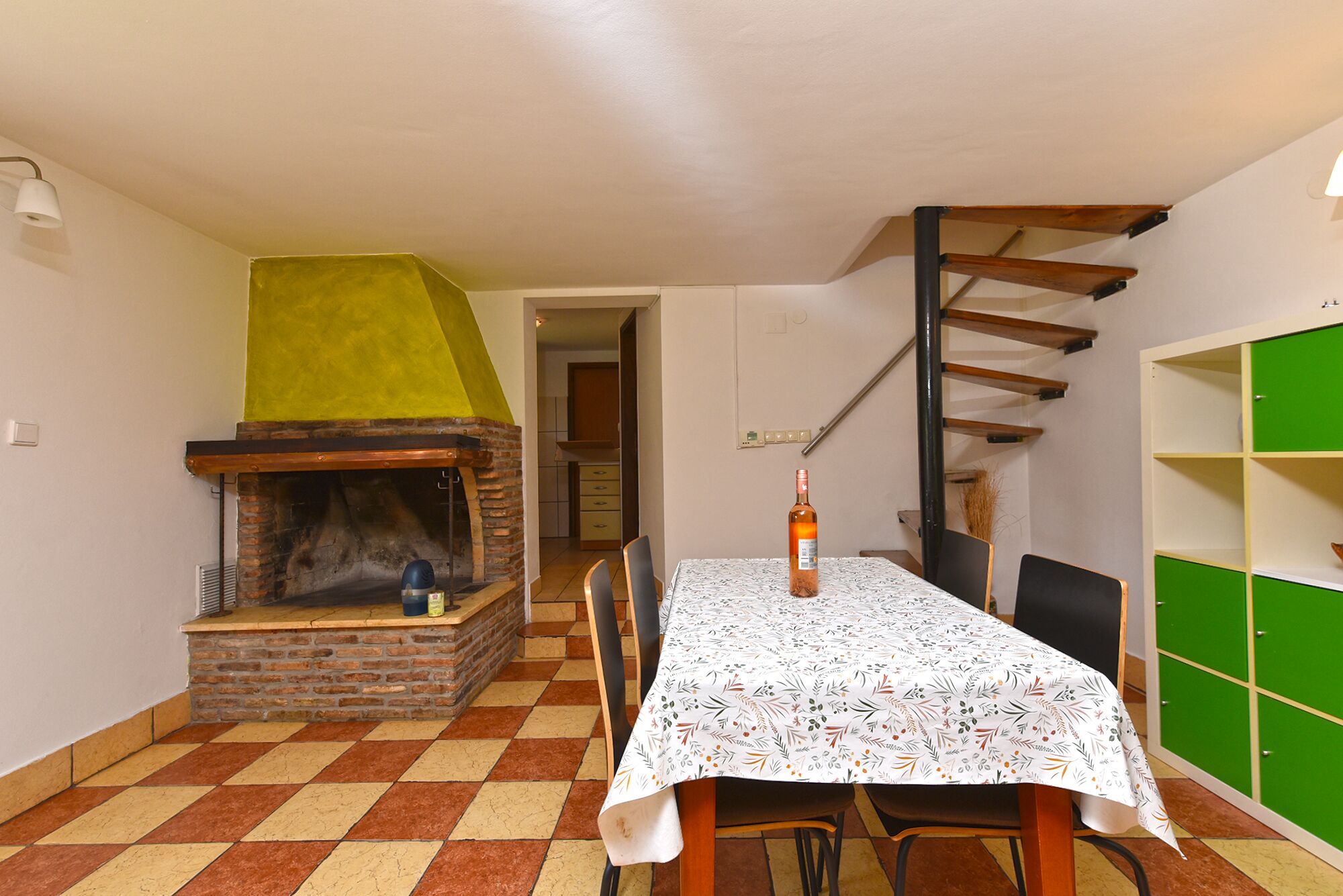 Un comedor con chimenea de ladrillo, una mesa con mantel floral y un armario verde.