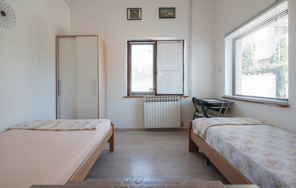 A small, clean room with two single beds, a radiator, a desk, and a window with blinds.