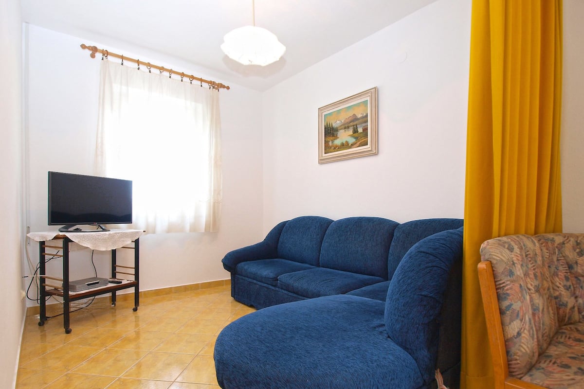 A living room with a blue sofa, a small table with a TV, a painting on the wall, and a yellow curtain.