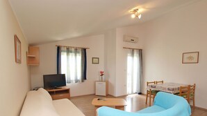 A cozy living room with a sofa, a TV, a small table, and a dining area with chairs. - Apartments Daffodils 1002 (Fazana)