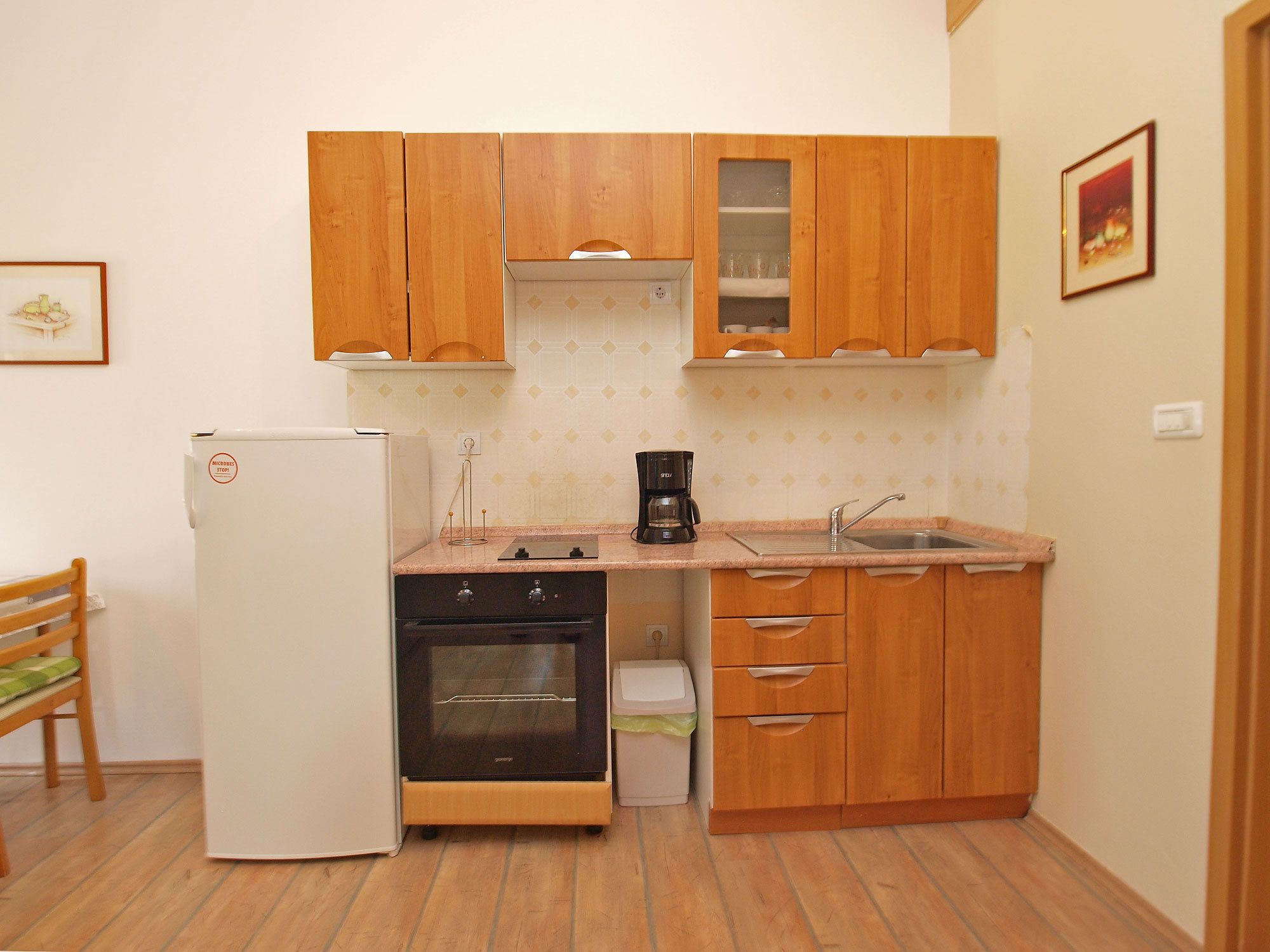 A compact kitchen with wooden cabinets, a built-in oven, a refrigerator, and a coffee maker.