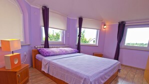 A bedroom with a bed, a nightstand, a lamp, and two windows with curtains. - Apartments Daffodils 1002 (Fazana)