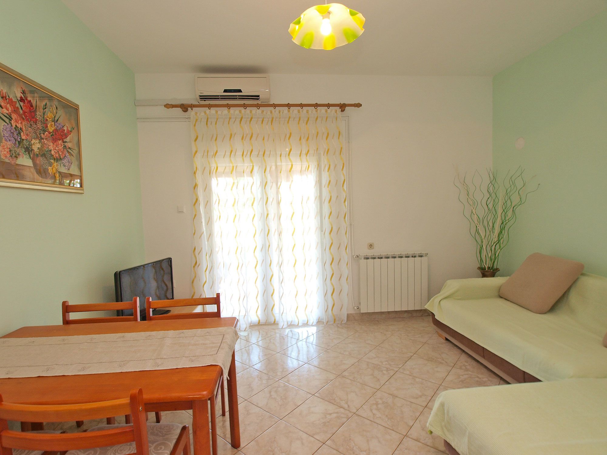 A living room with a dining table, chairs, a sofa, a radiator, a ceiling fan, and a window with curtains.