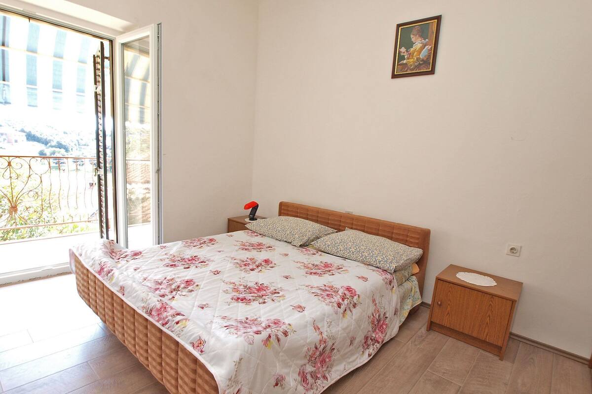 A bedroom with a bed, a nightstand, a painting, and a view through a window.