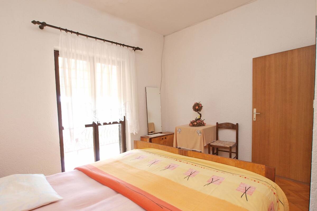 A bedroom with a bed, a bedside table, a chair, a wooden wardrobe, and a window with curtains.