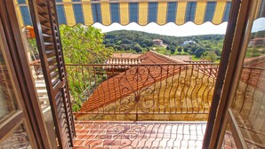 Ein Balkon mit schmiedeeisernem Gitter, Fliesenboden und Blick auf eine ländliche Landschaft mit Häusern und Bäumen.