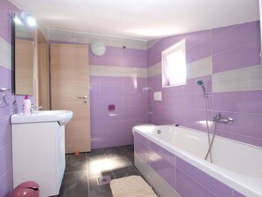 Une salle de bain avec des carreaux violets, une baignoire blanche, un lavabo et un miroir.