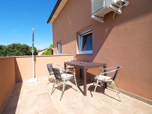 Une terrasse extérieure avec une table et des chaises, un mât de drapeau et un bâtiment doté d’une fenêtre et d’un appareil de climatisation.