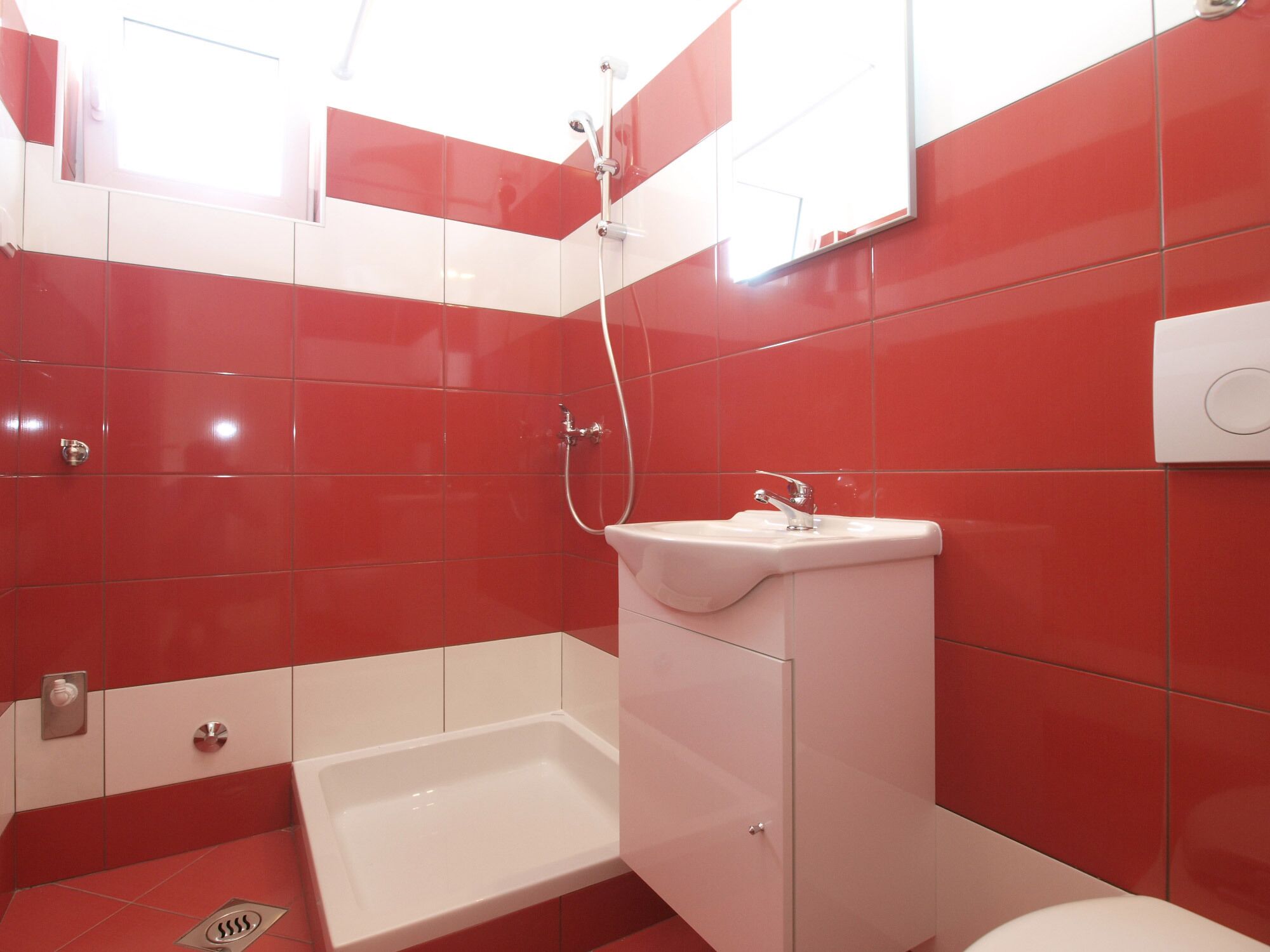 A bathroom with red and white tiles, a white sink, and a shower.
