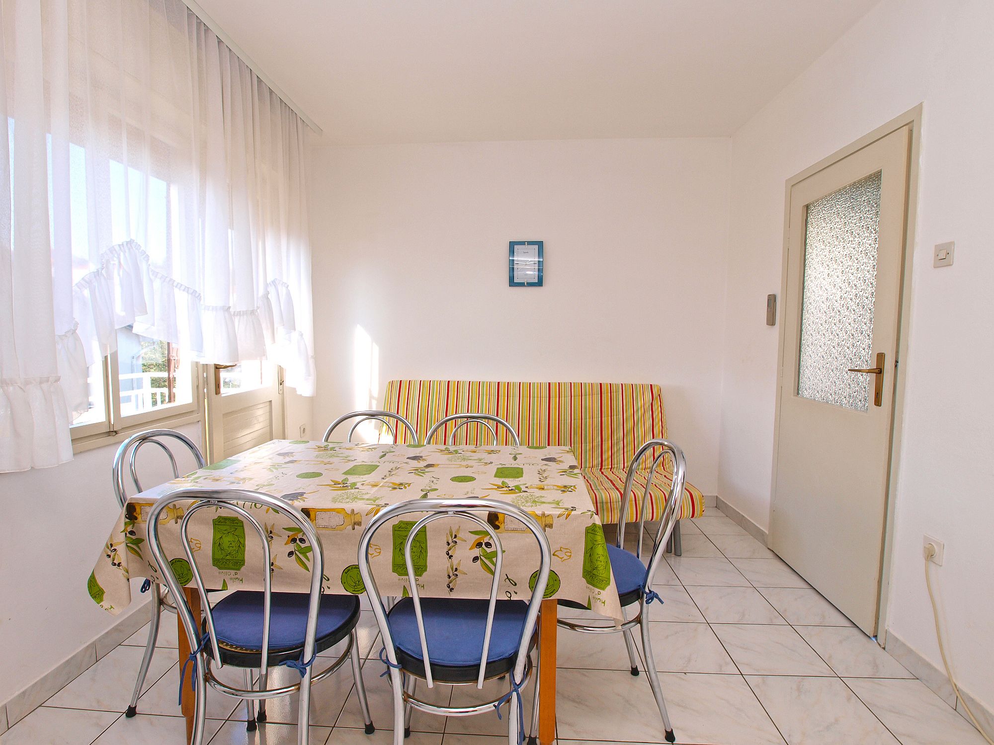 Zona pranzo con tavolo ricoperto da tovaglia a motivi floreali, circondata da quattro sedie con cuscini blu.